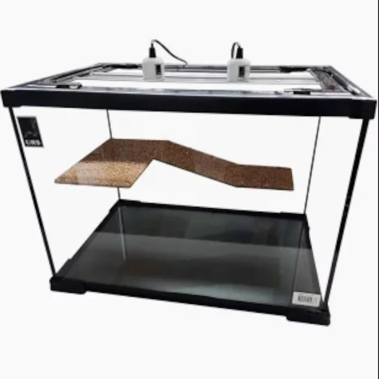 Rectangular glass aquarium on a black frame with a zigzag brown wooden ramp suspended inside; two white devices sit on top.